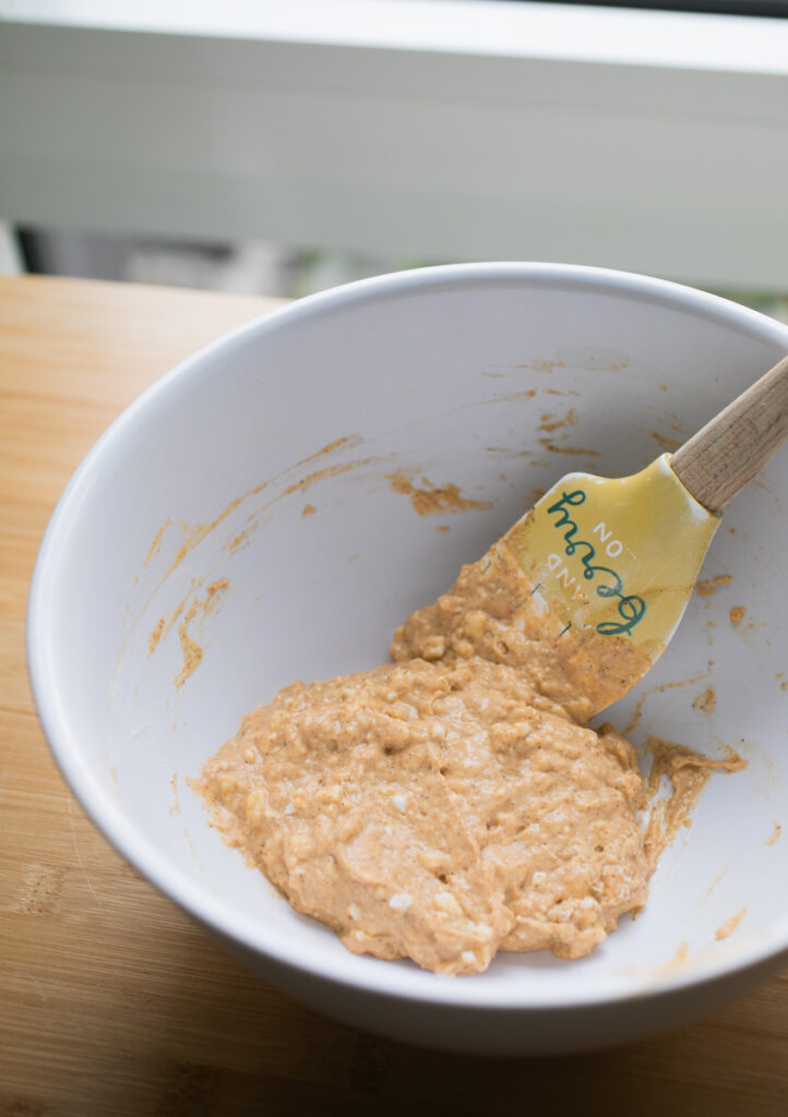 Very thick pumpkin cottage cheese pancake batter in a white bowl with a spatula.