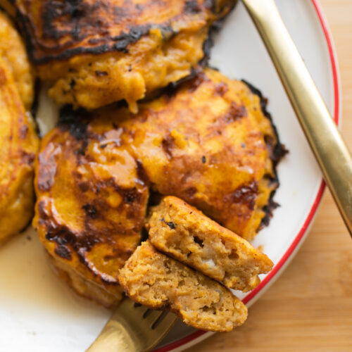 a fork holding up a bite of pumpkin pancakes on a white plate.