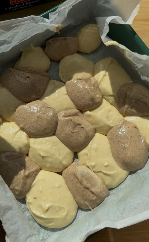 A square baking pan holding alternating dollops of brown and white batter.