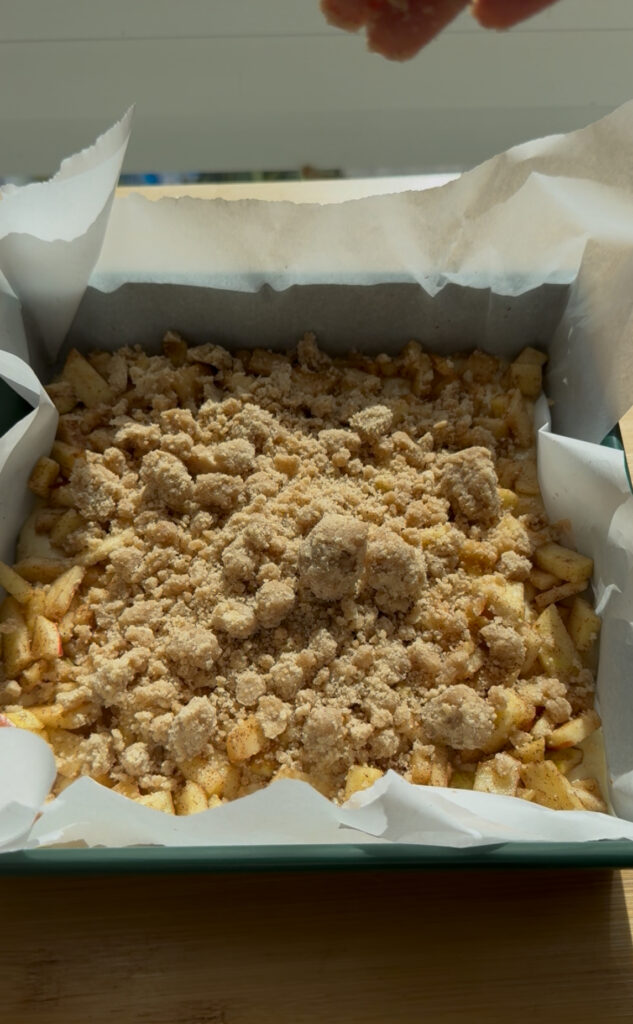 A square baking pan filled with cake batter topped with apples and crumbs.