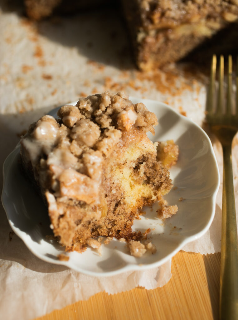 A slice of apple crumb cake on a white plate with a bite taken out of it to show the close crumb.