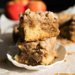 Two squares of apple crumb cake stacked on top of each other on a white plate.