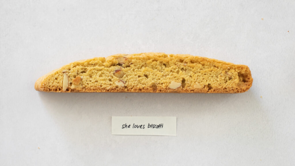 A pice of biscotti on a gray background with the label "She Loves Biscotti."