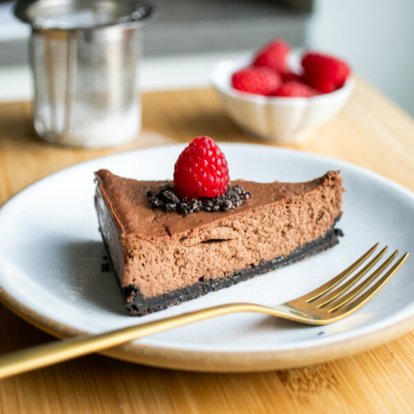 A slice of chocolate cheesecake on a white plate topped with a raspberry.