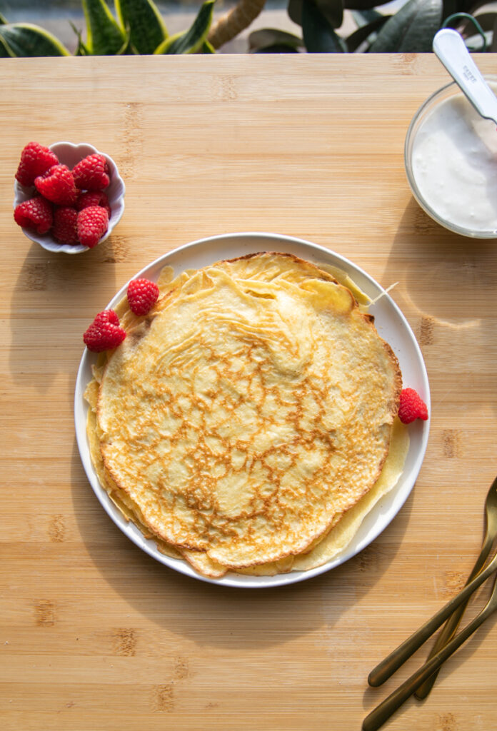 A white plate of crepes with raspberries.
