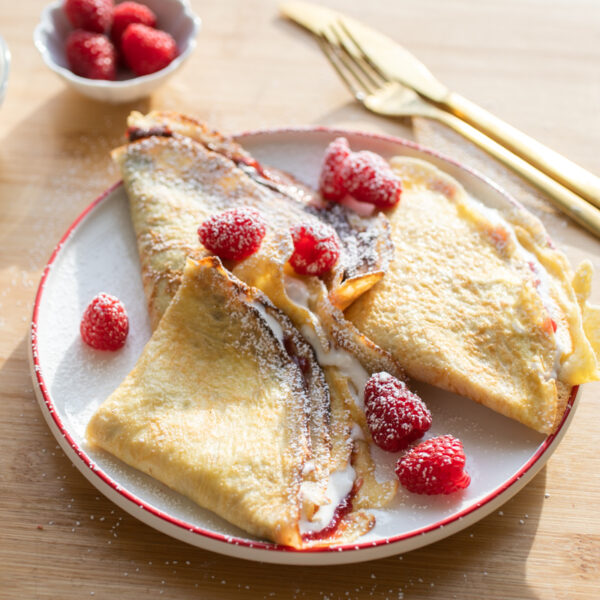 Three crepes with raspberries on a white plate.