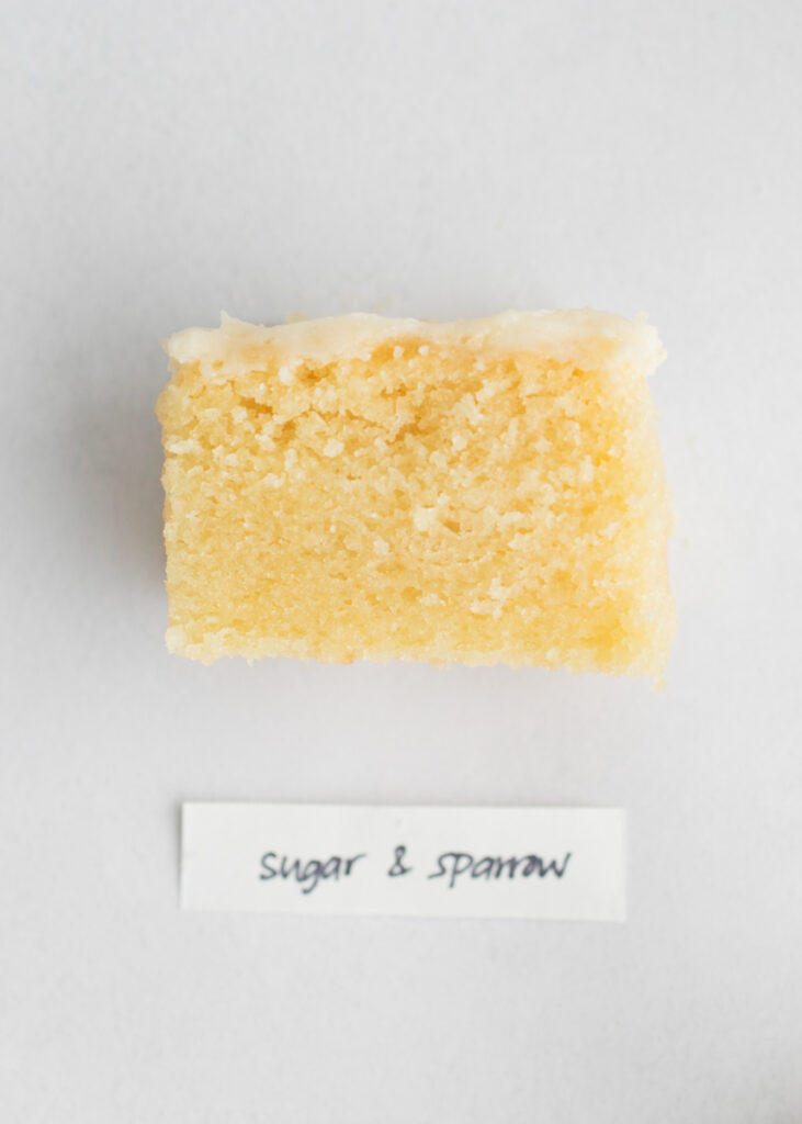 A slice of vegan vanilla cake with a label that says "Sugar and Sparrow."