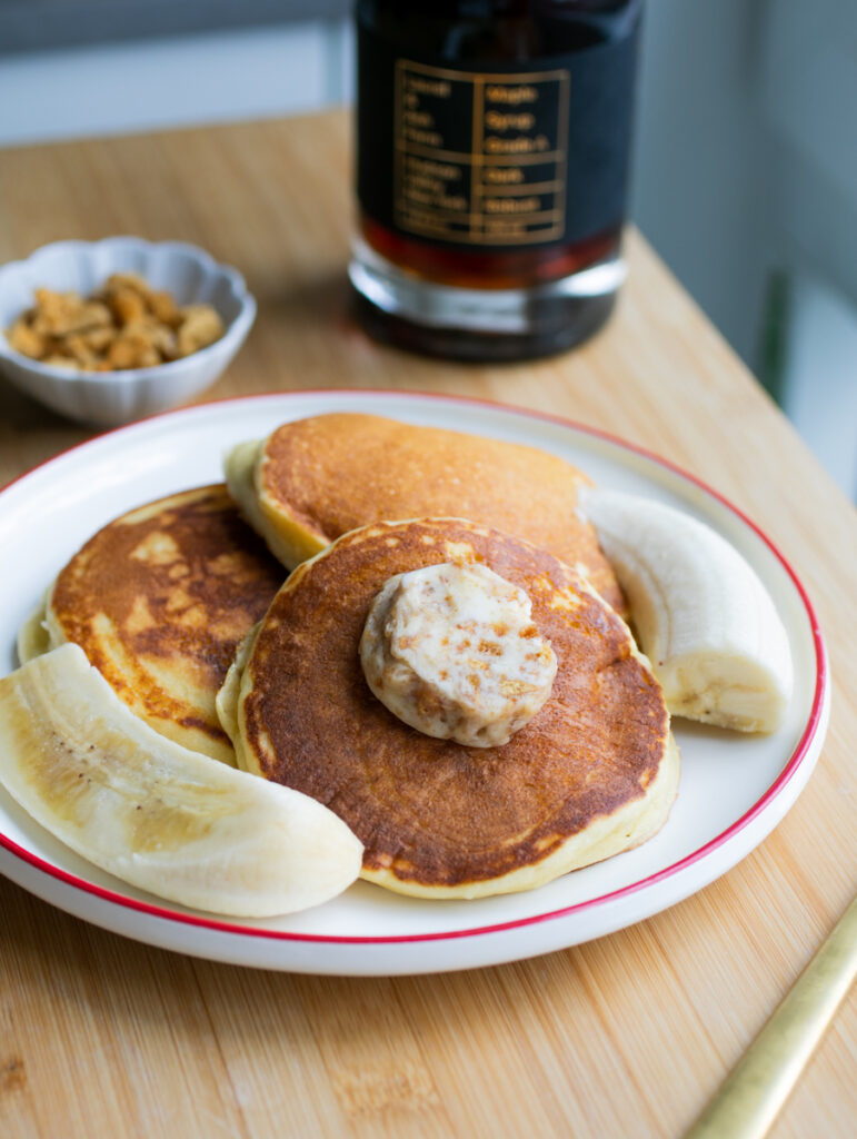 Three fluffy pancakes on a plate with banana halves.