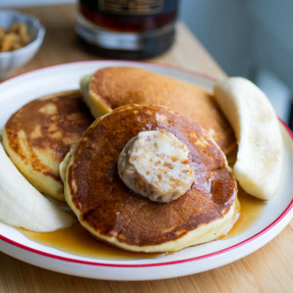 Three fluffy pancakes on a plate with banana halves.
