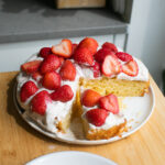 A cornmeal cake topped with a Greek yogurt frosting and cut strawberries.