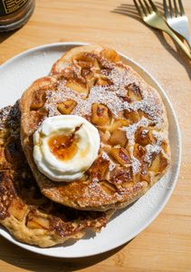Two large apple pancakes on a white plate topped with a dollop of yogurt.