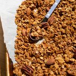 Granola spread out on a sheet of parchment with spoon.