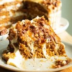 A slice of pumpkin cake on a plate with a bite taken out to reveal the close crumb.